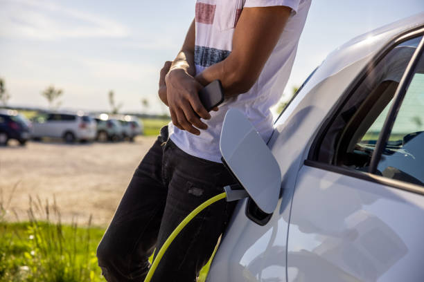 istock Man holding mobile phone while charging electric car outdoors 1354069919