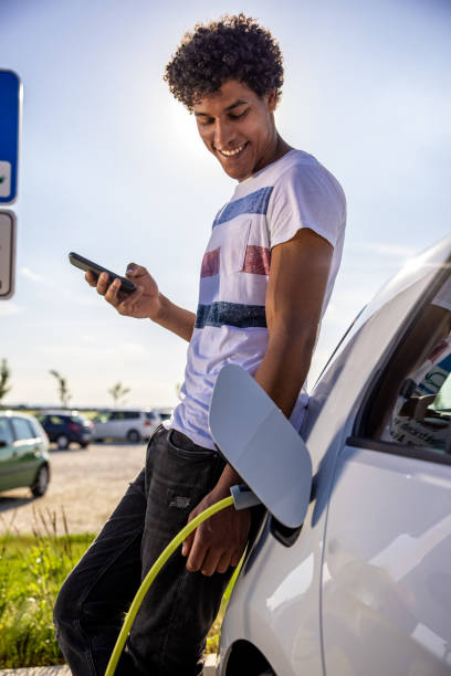 istock Man using mobile phone while charging electric car outdoors 1354069943