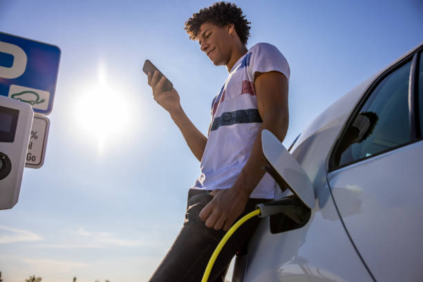 istock Man texting on smart phone while charging electric car outdoors 1354069950