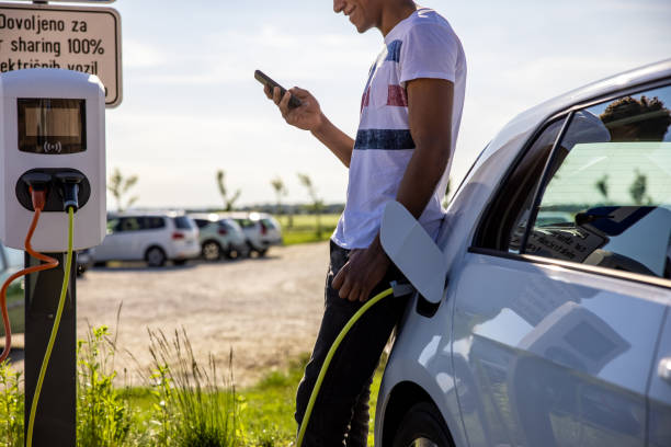 istock Man using mobile phone while charging electric car outdoors 1354069979