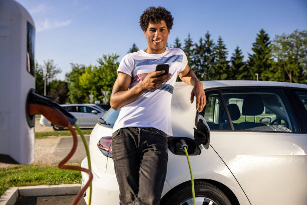 istock Man texting on smart phone while charging electric car outdoors 1354070007