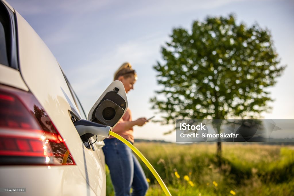 Woman using mobile phone while charging electric car - Royalty-free Elektrikli Araba Stok görsel