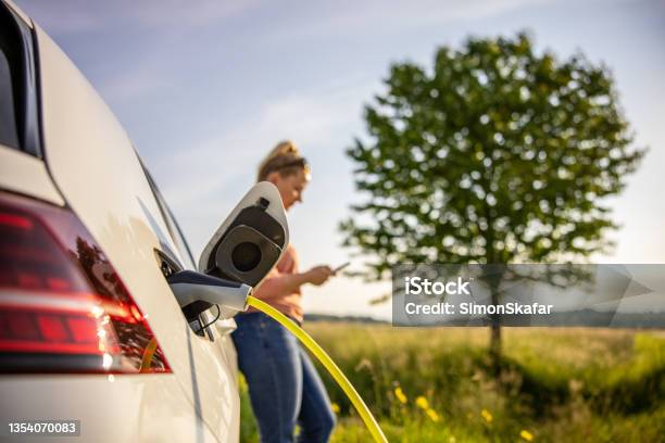 Woman Using Mobile Phone While Charging Electric Car Stok Fotoğraflar & Elektrikli Araba‘nin Daha Fazla Resimleri