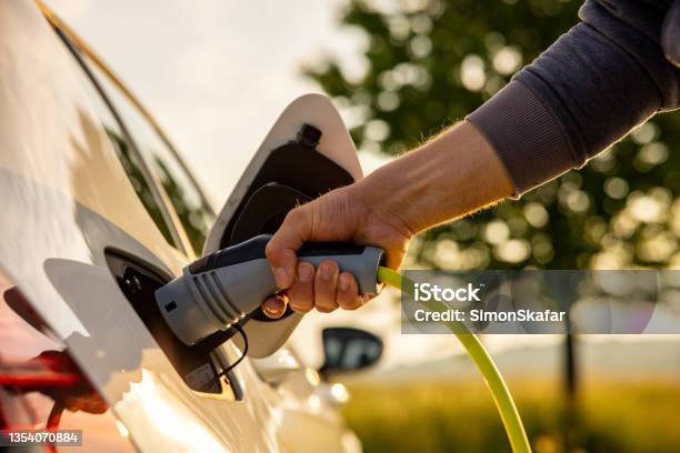 Man Inserts A Power Cord Into An Electric Car For Charging In The Nature Stock Photo - Download Image Now