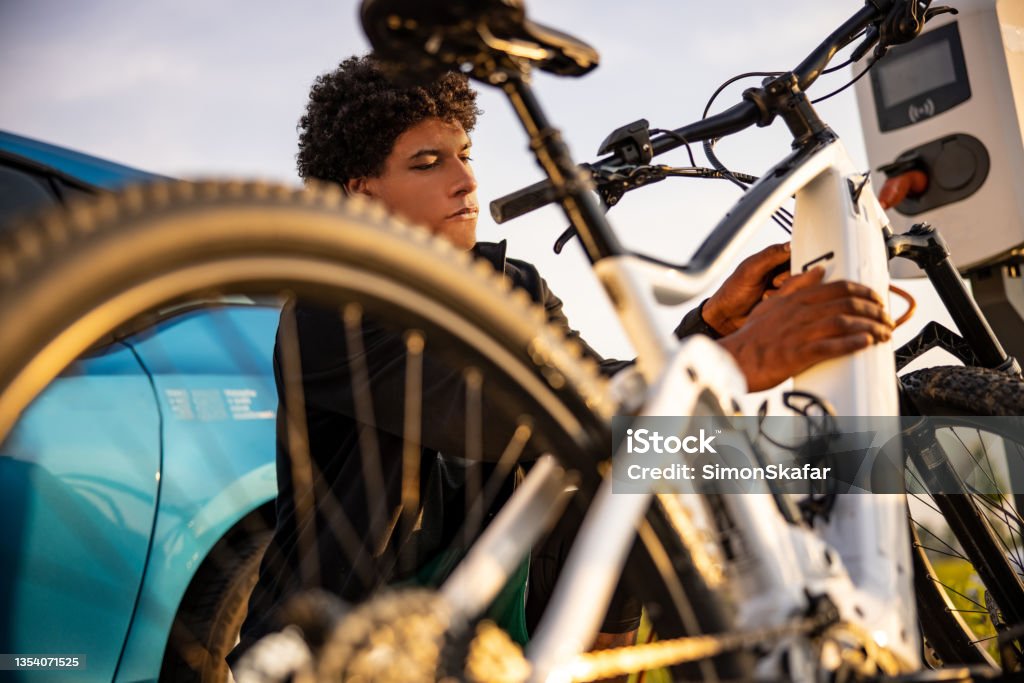 Young man inserting plug into electric bicycle for charging Young man inserting plug into electric bicycle for charging at electric charging station Electric Bicycle Stock Photo