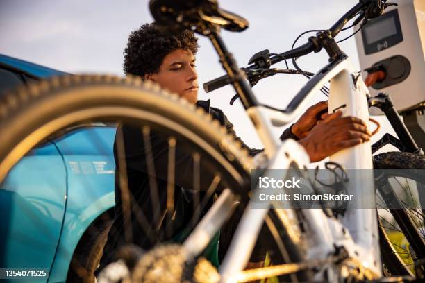 Young Man Inserting Plug Into Electric Bicycle For Charging Stock Photo - Download Image Now