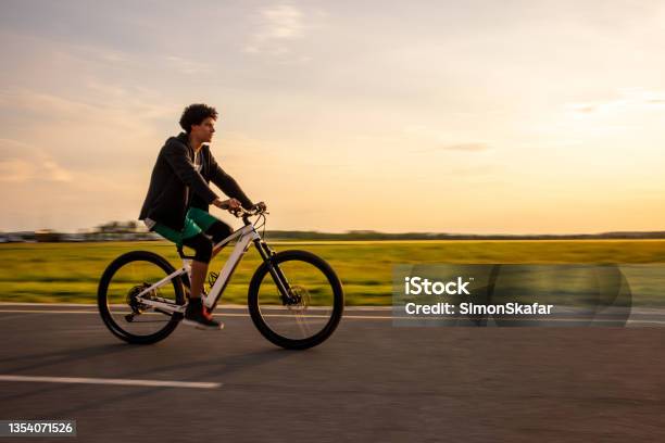Young Man Riding Electric Bicycle On Rural Road Stock Photo - Download Image Now - Electric Bicycle, African Ethnicity, Bicycle