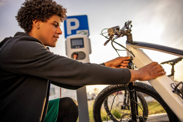 istock Happy young man inserting plug into electric bicycle for charging 1354071577