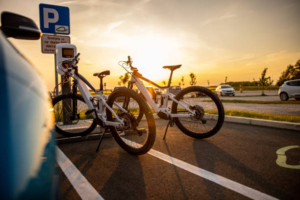 Two electric bicycles being charged at the electric vehicle charging station Two electric bicycles being charged at the electric vehicle charging station on parking lot during sunset electric bicycle stock pictures, royalty-free photos & images