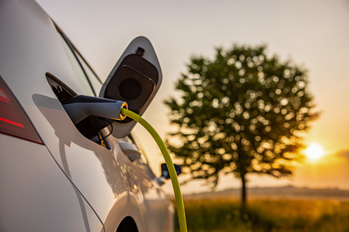 Charging an electric car on rural field during sunset