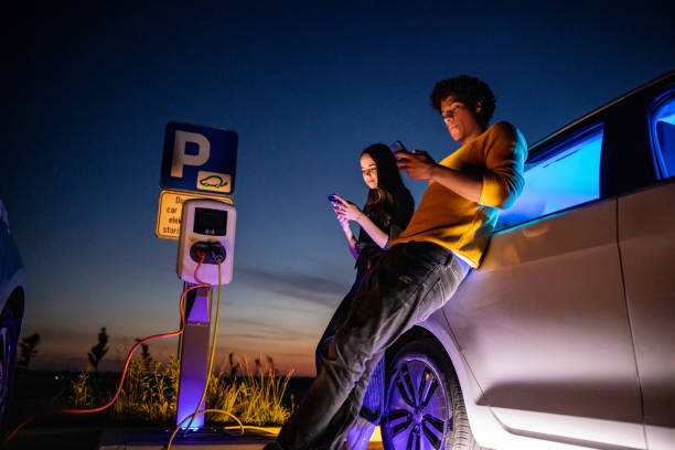 istock Couple using mobile phones while their electric car is charged 1354072937