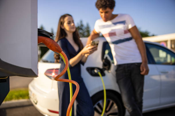 istock Couple using mobile phone while their electric car is charged 1354072993