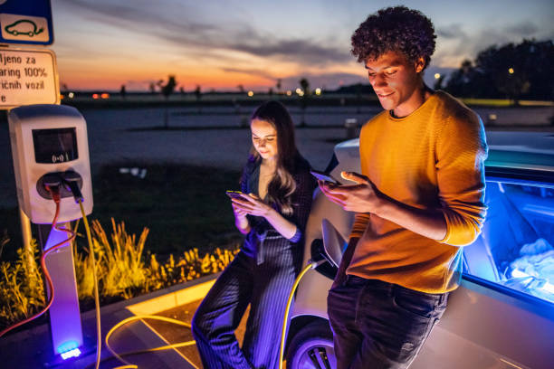 istock Couple using mobile phones while their electric car is charged 1354072998