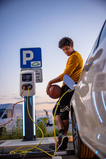 Basketball player waiting while his electric car is charged African american basketball player waiting for his EV car to be charged at charging station battery charger photos stock pictures, royalty-free photos & images
