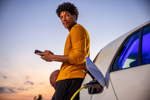 istock Portrait of basketball player using mobile phone while charging electric car 1354073755