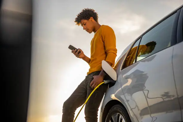 Photo of Man using mobile phone while charging electric car
