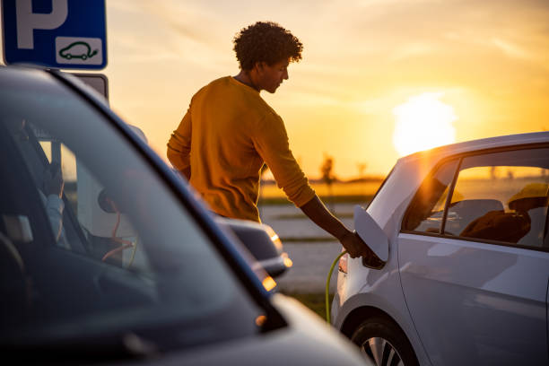 afroamerikaner steckt stecker in die ladebuchse des elektroautos - benzin sparen stock-fotos und bilder