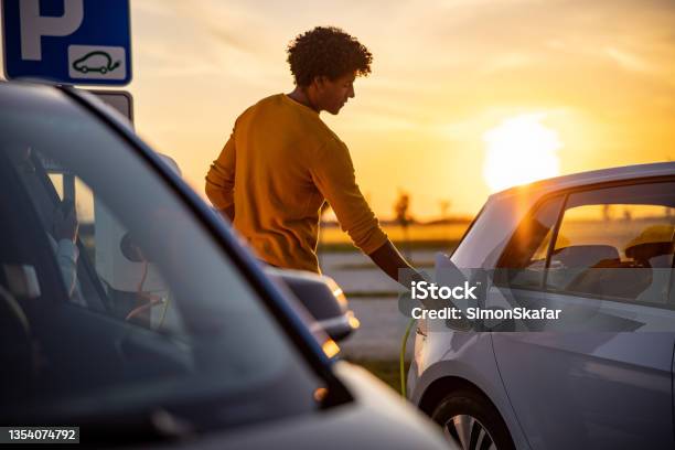 African American Man Inserting Plug Into The Electric Car Charging Socket Stock Photo - Download Image Now