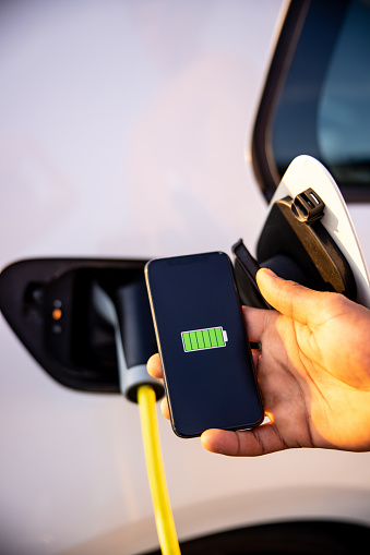 Charging modern electric car with mobile phone screen showing full battery charged sign