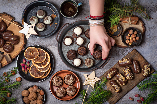 Woman serving luxurious, homemade chocolate praline candies, different shapes in bowls on a rustic gray background with Christmas decorations top view