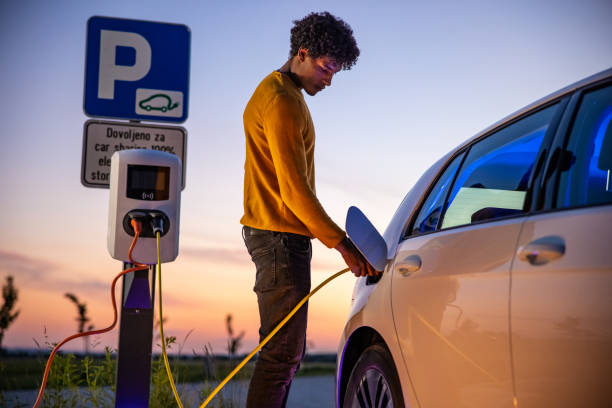 african american man inserting plug into the electric car charging socket - elektrikli araba lar stok fotoğraflar ve resimler