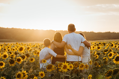 Parents with children looking at view while standing in sunflowers field against sky