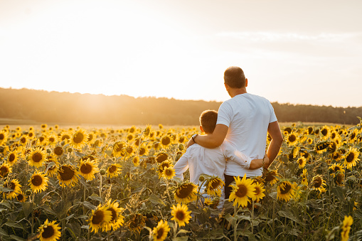 Father and son looking at view while standing in sunflowers field against sky