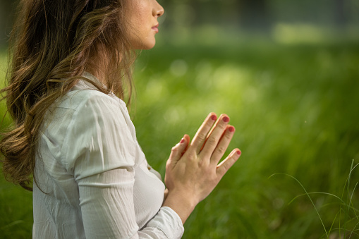 Midsection of woman meditating with joined hands in forest