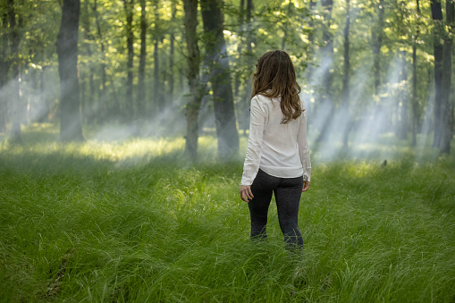 Rear view of woman walking on grass in forest