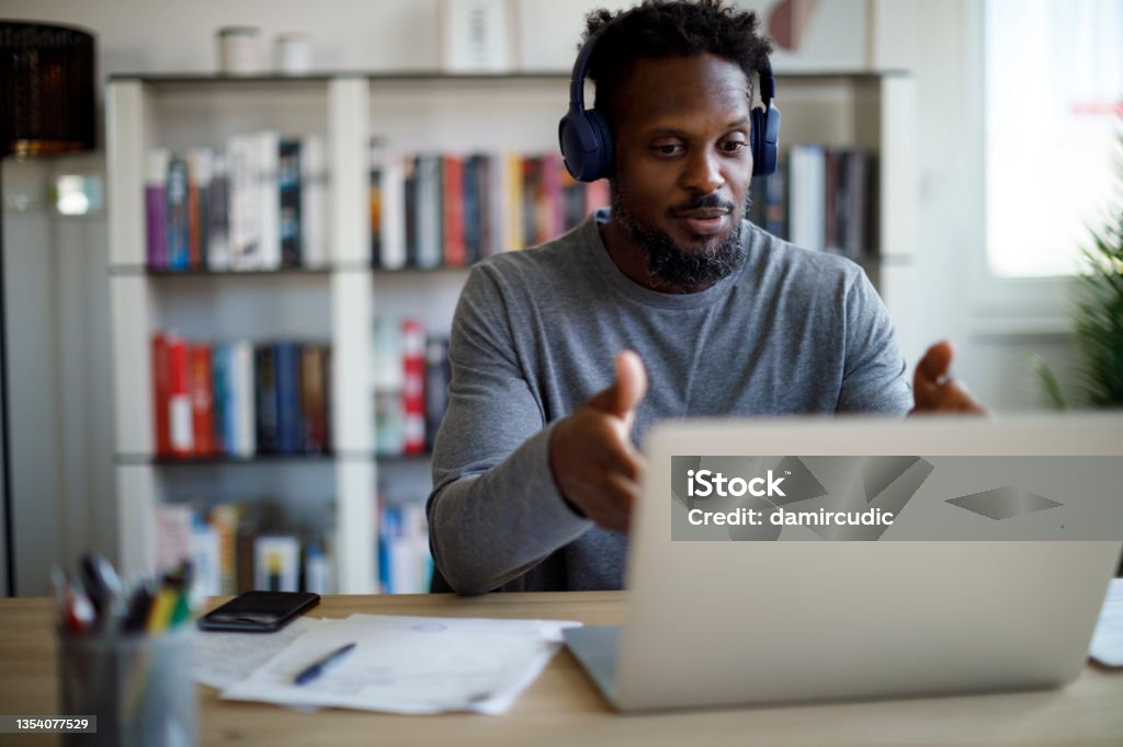 Man with bluetooth headphones having video call on laptop computer in his home office Education Training Class Stock Photo
