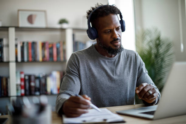istock Man with bluetooth headphones having video call on laptop computer in his home office 1354077577