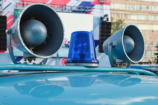 Details of retro police car with a megaphone and flashing blue siren light mounted on top. Loud-hailers on police car for message information at emergency. Vintage loudspeakers on car roof.