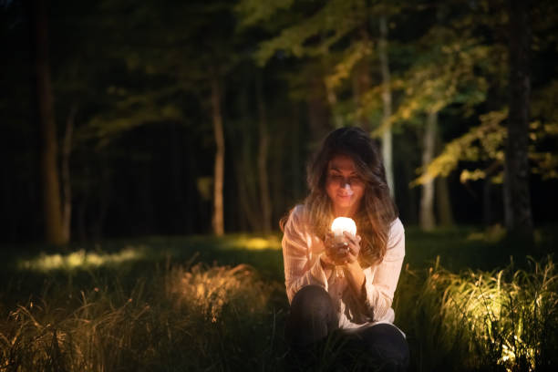 istock Beautiful woman crouching and holding glowing object with eyes closed 1354078883