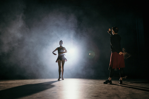 Ballet teacher teaching ballet dancers on stage illuminated with lights