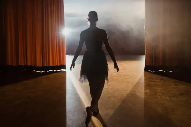 Rear view of ballerina walks into the stage after the curtains open of theater