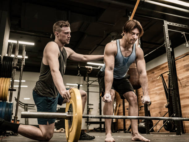istock Young Man lifting weights with his trainer in the Gym 1354080575