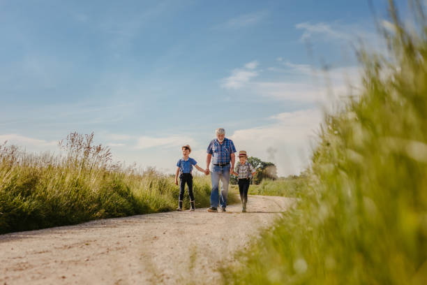istock Grandfather with grandsons walking on dirt road against clouds 1354081392