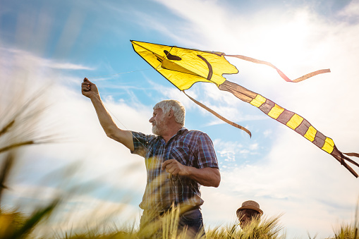 Senior man flying kite while standing in agricultural field against cloudy sky