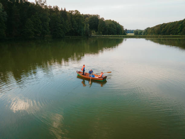 Grandfather with grandsons fishing on a boat at lake Grandfather with grandsons sitting in rowing boat fishing on lake at park rowing boat fishing stock pictures, royalty-free photos & images