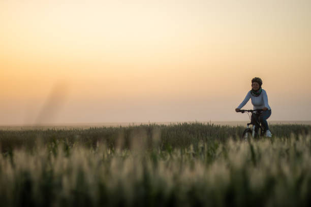 Female cyclist riding bicycle on field during sunset