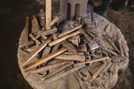 Metal and wooden tools of blacksmith on wooden object at workshop