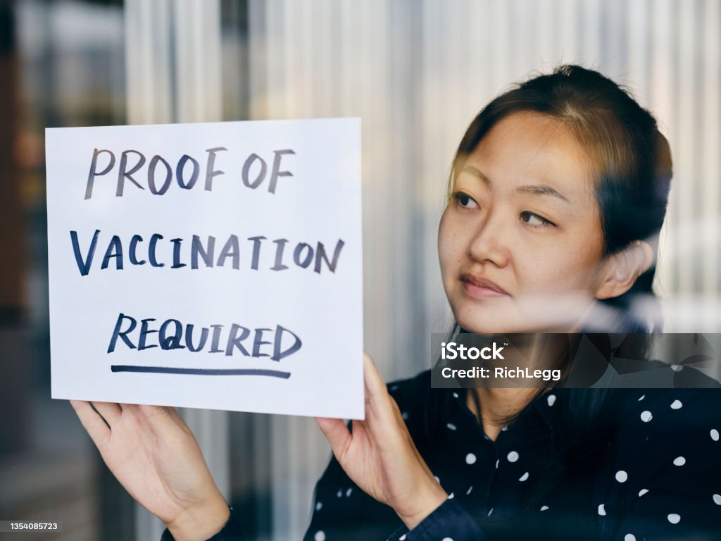 Business Owner Wtih Vaccine Mandate Sign A business owner putting up a sign requiring proof of vaccination. Vaccination Stock Photo
