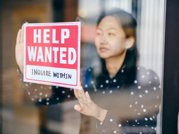 Business Owner Putting Up Help Wanted Sign A small business owner, putting up a help wanted sign in her store window. help wanted sign stock pictures, royalty-free photos & images
