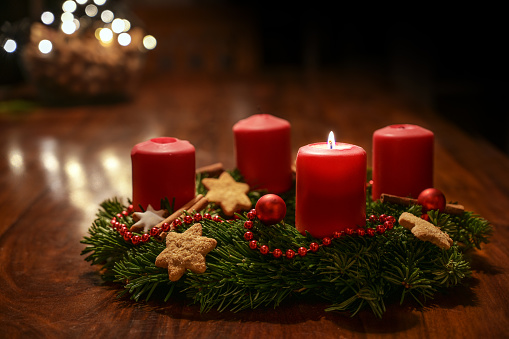 Primer Adviento: corona de Adviento decorada de ramas de abeto con velas rojas encendidas en una mesa de madera en el tiempo antes de Navidad, bokeh festivo en el cálido fondo oscuro, espacio de copia, enfoque seleccionado photo