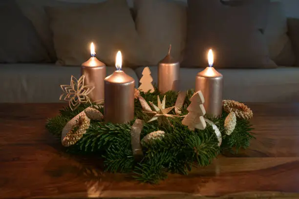 Third Advent with three lit golden candles on an Advent wreath with natural Christmas decoration on a wooden coffee table, copy space, selected focus, narrow depth of field