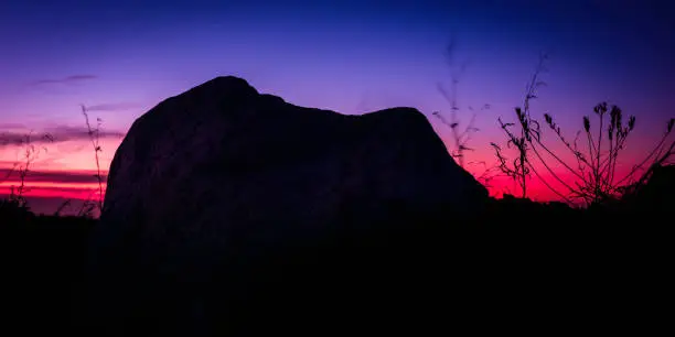 Abstract geometry of curving shape of rock against red, orange, blue and purple sky background. Silhouette natural settings on the mountain top in Bourne, Massachusetts.