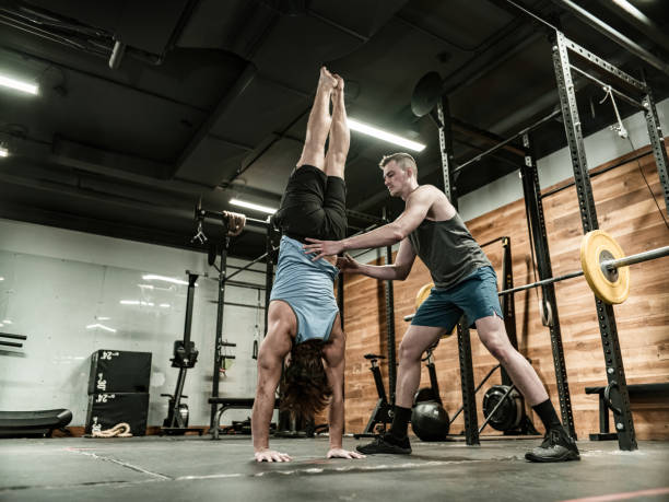 istock Young Man doing a handstand with trainer  in the Gym 1354092074