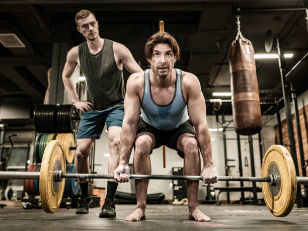 istock Young Man lifting weights with his trainer in the Gym 1354092973