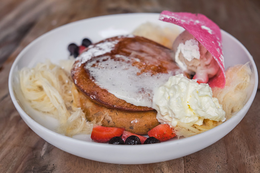 Close-up shot of healthy vegan protein hotcake with mixed berries, candy floss, vanilla ice cream and custard