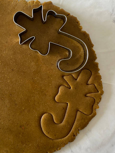 nahaufnahme von hausgemachtem, auf fettfestem pergamentpapier ausgerolltem lebkuchenteig mit zuckerstangen-keksschneider aus metall, zuckerrohr mit ausgeschnittenen schleifenformen, hausbacken, erhöhte sicht - candy cane christmas cookie raw food stock-fotos und bilder